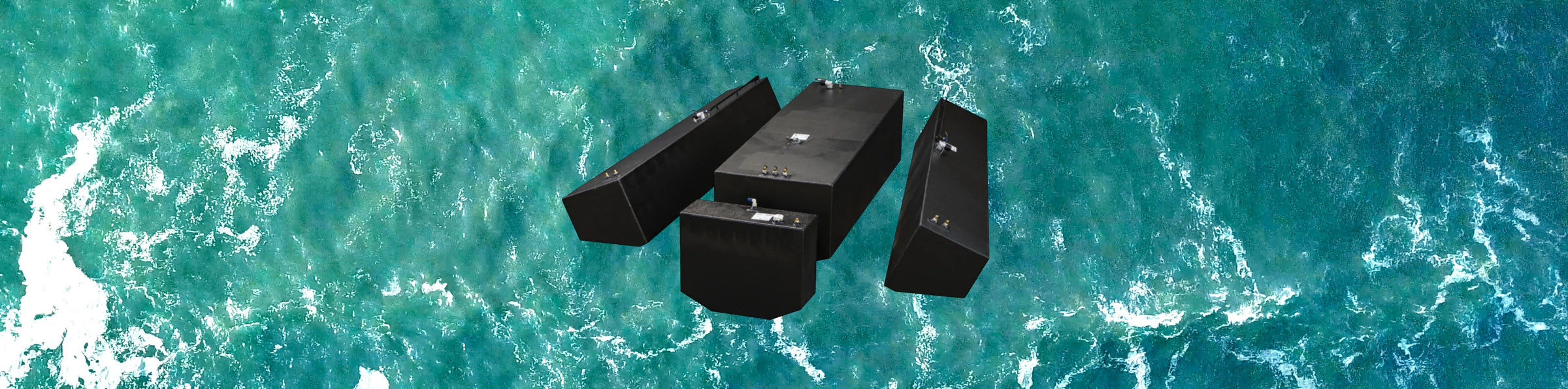 An aerial view of four black OEM replacement fuel tanks floating on the ocean, surrounded by turquoise water with white foam.