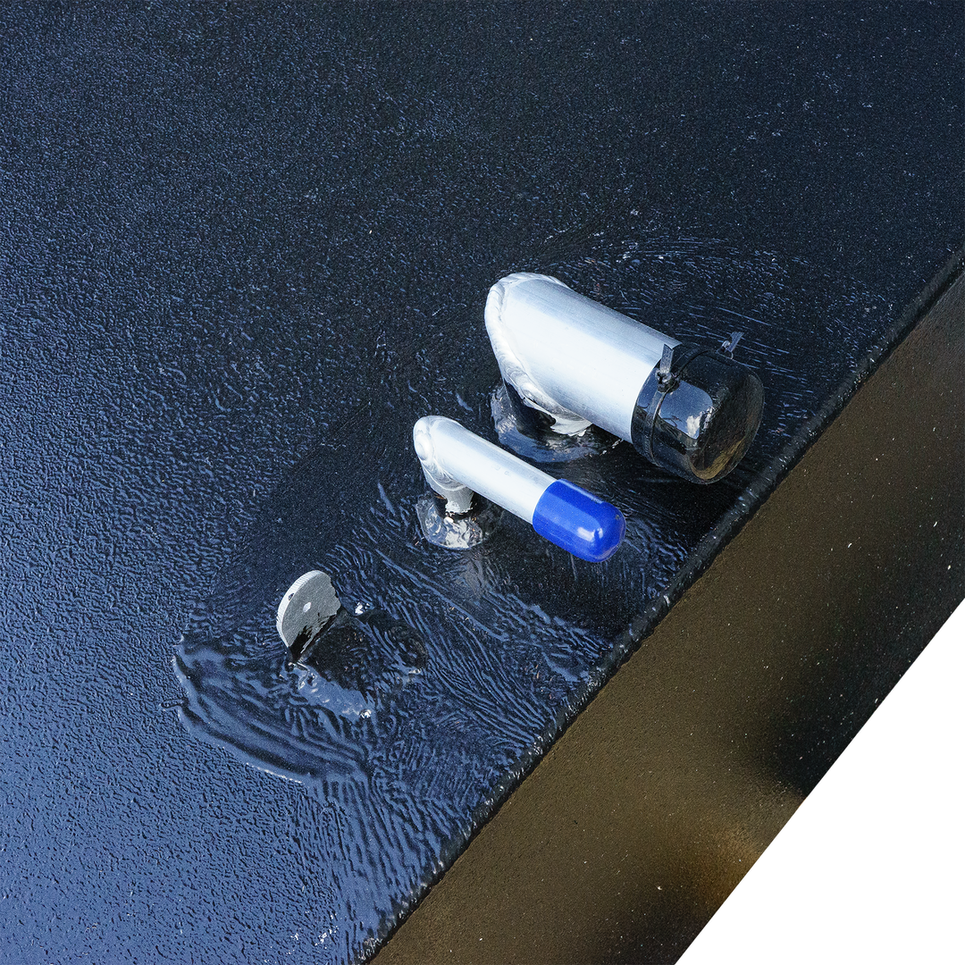 Close-up view of a 2001 Century Boats 254 belly fuel tank featuring two fuel fittings, one with a blue cap and another with a black cap, on a textured black surface