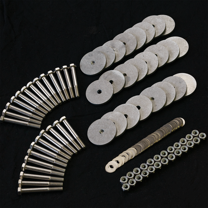 A collection of metal hardware components arranged on a black surface, including three curved rows of large, flat, circular washers with central holes, two sets of long, shiny bolts with hexagonal heads, a row of smaller flat washers, a set of small cylindrical spacers, and a row of nuts