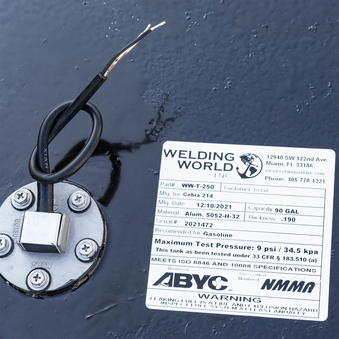 A white product label for a fuel tank from "WELDING WORLD INC." is adhered to a black, textured surface. The label provides details about the tank: Part # WW-T-250, Mfg. for Cobia 214, Mfg. Date: 12/10/2021, Capacity: 90 GAL, Material: Alum. 5052-H-32, Thickness: .190, Serial #: 2021472. It is recommended for Gasoline and has a Maximum Test Pressure of 9 psi / 34.5 kpa. The tank has been tested under 33 CFR § 183.510 (a) and meets ISO 8846 and 10088 SPECIFICATIONS