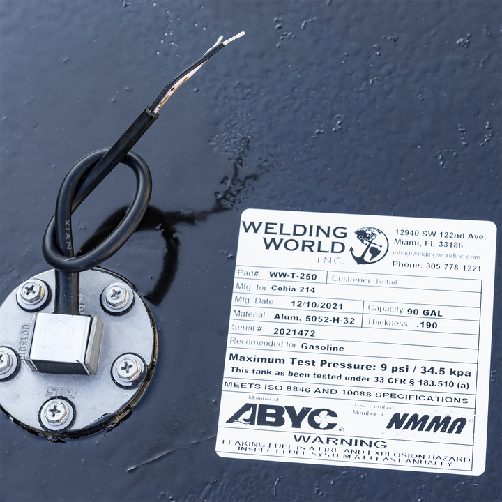 A white product label for a fuel tank from "WELDING WORLD INC." is adhered to a black, textured surface. The label provides details about the tank: Part # WW-T-250, Mfg. for Cobia 214, Mfg. Date: 12/10/2021, Capacity: 90 GAL, Material: Alum. 5052-H-32, Thickness: .190, Serial #: 2021472. It is recommended for Gasoline and has a Maximum Test Pressure of 9 psi / 34.5 kpa. The tank has been tested under 33 CFR § 183.510 (a) and meets ISO 8846 and 10088 SPECIFICATIONS