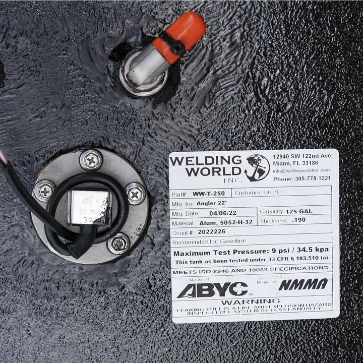 A white product label from "Welding World Inc." affixed to a textured black surface. The label provides details for a "WW-T-250" fuel tank for an "Angler 22'", manufactured on 04/06/22, made of Alum. 5052-H-32 with a thickness of .190, and a capacity of 125 gallons. It also specifies a maximum test pressure of 9 psi / 34.5 kpa and lists compliance with ISO 8846 and 10088 specifications. To the left of the label