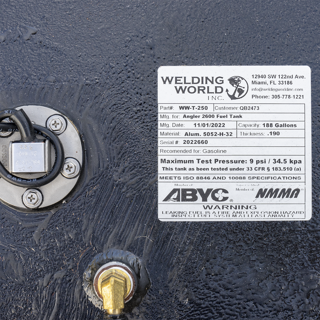 A close-up of a white manufacturer's label on a black, textured fuel tank. To the left of the label is a round, silver fuel sending unit, and a large brass fitting is visible below it. The "Welding World, Inc." label identifies the product as an "Angler 2600 Fuel Tank" with a capacity of 188 gallons, manufactured on November 1, 2022. The label also displays ABYC and NMMA compliance logos above a safety warning