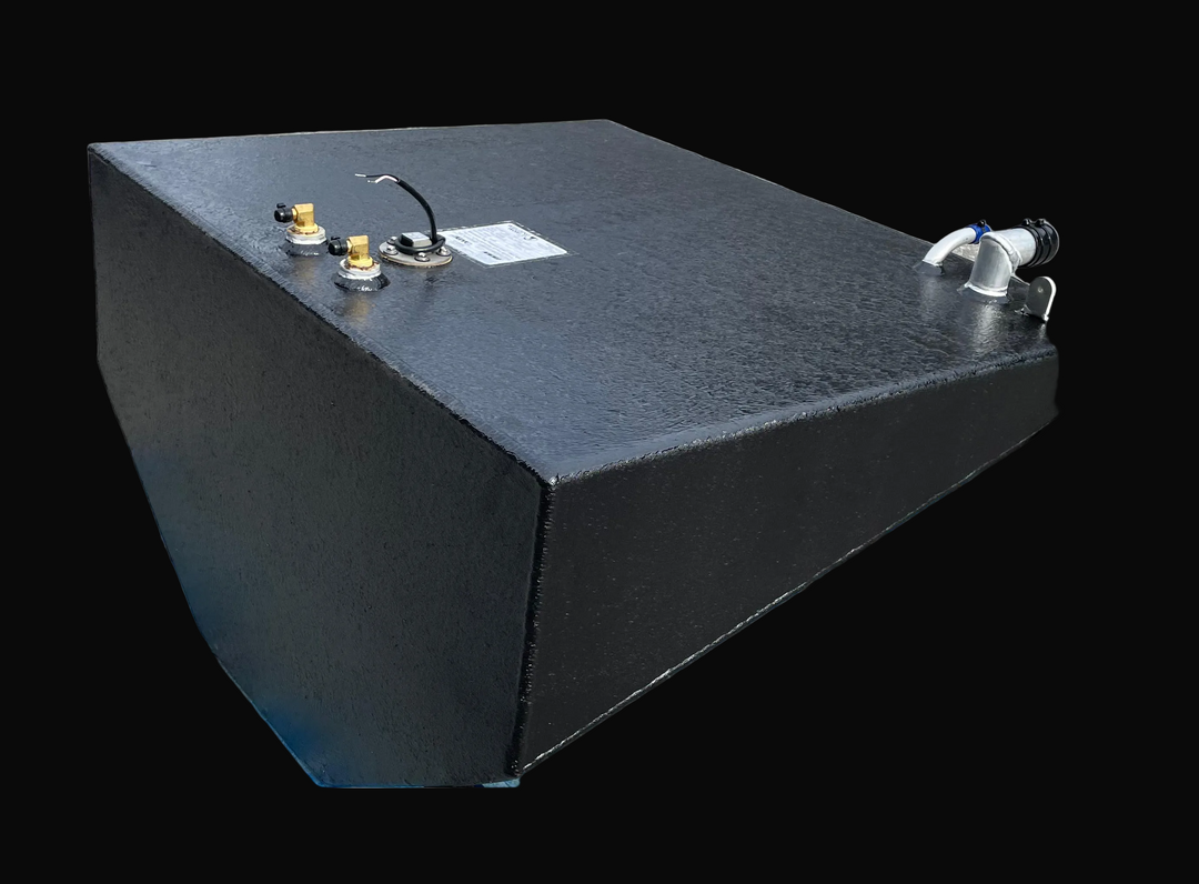 A detailed angled photograph of a wedge-shaped center marine fuel tank with a textured black finish and a V-shaped bottom. The flat top surface is populated with several brass fittings, a black electrical lead, a technical specification label, and a silver-toned fill neck assembly located on the right side.