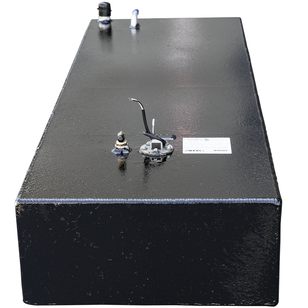A long, black, rectangular fuel tank with a textured surface, shown from a slightly elevated perspective. The top of the tank features various metal fittings, including a hose connection, a black post, a circular gauge with wires and a white label, and a small golden-colored post