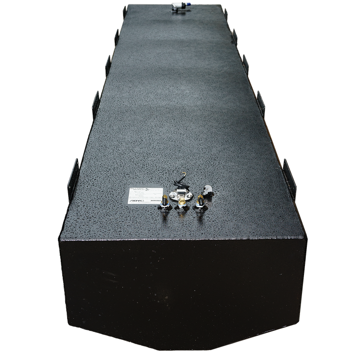 A long, black, rectangular fuel tank with a textured surface is shown from an elevated perspective. The tank, which is a Baja 280 1990 - 204 gal. OEM replacement belly fuel tank (short version), has various metal fittings and connections on its top surface, including a white label with text and small tubes. Mounting brackets are visible along the sides of the tank. The front end of the tank is subtly rounded. The background is a checkered pattern of black and transparent squares