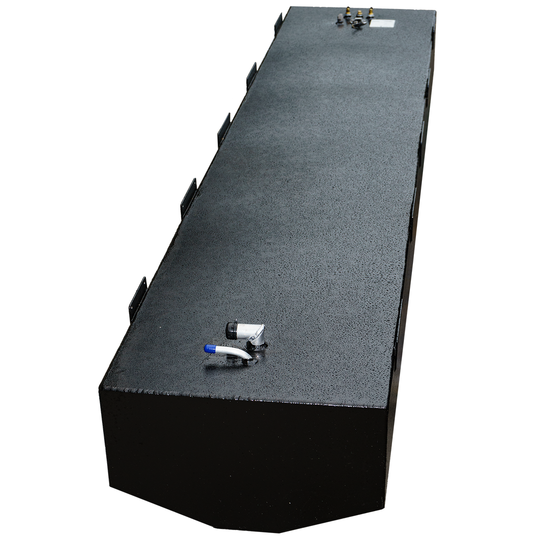 A long, black, rectangular fuel tank with a textured surface, shown from an elevated, angled perspective. It features various metal fittings and connections on its top surface, including a blue-capped tube and a set of brass-colored fittings on the far end. Multiple mounting brackets are visible along the sides of the tank. The front end of the tank is subtly rounded. The background is a checkered pattern of black and transparent squares.