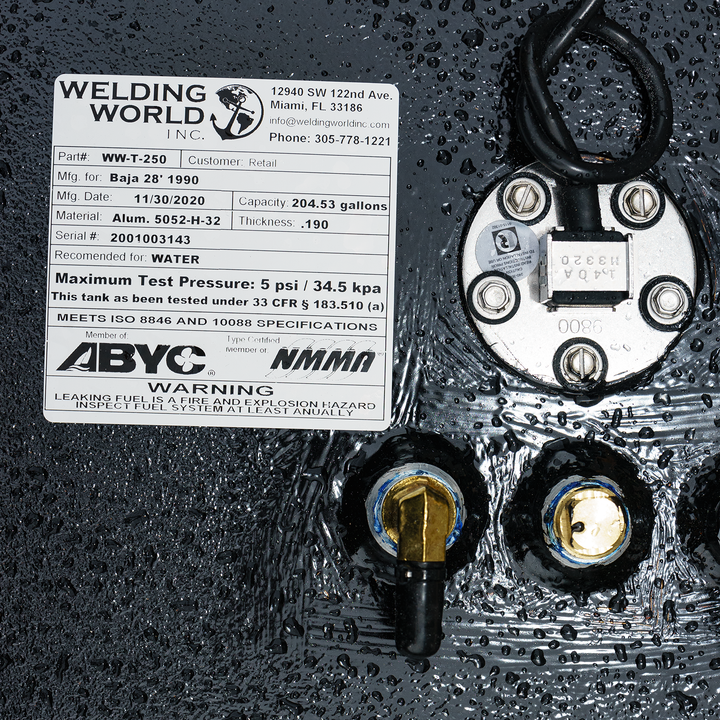 A close-up shot of a white rectangular product label from "Welding World Inc." affixed to a textured black surface, possibly a fuel tank, which appears wet with water droplets. The label provides detailed specifications for a tank designed for a Baja 28' 1990, manufactured on 11/30/2020, with a capacity of 204.53 gallons. It's made of Aluminum 5052-H-32 with a thickness of .190 and has a serial number 2001003143. The tank is recommended for WATER and has a maximum test pressure of 5 psi / 34.5 kpa