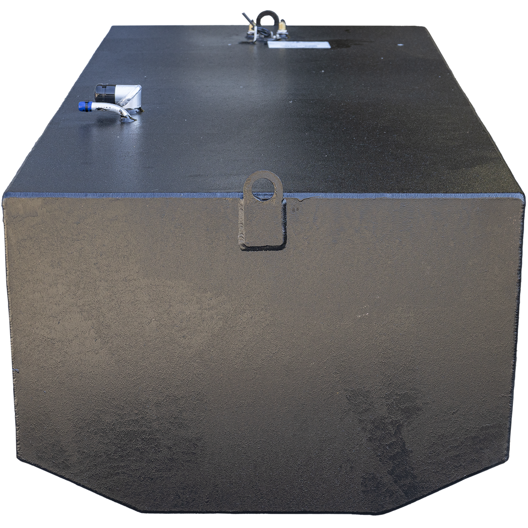 Black rectangular marine fuel tank with flat top and angled front bottom corners. The tank has a welded lifting eye in the center front, fittings including white and black pipes with blue caps on the top left, and a label mounted near the center back. The surface shows texture and welding marks. The background is transparent