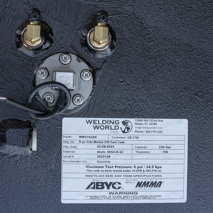 Black marine fuel tank surface with brass fittings and electrical wiring near a round metal plate. Below is a white label showing Welding World logo, part number WW316250, customer QB 2700, made for High Tide Marine 230 fuel tank, dated 02/28/2023, capacity 230 gallons, aluminum material, .190 thickness, serial number 2023156, certified by ABYC and NMMA, with safety warning about fuel leaks