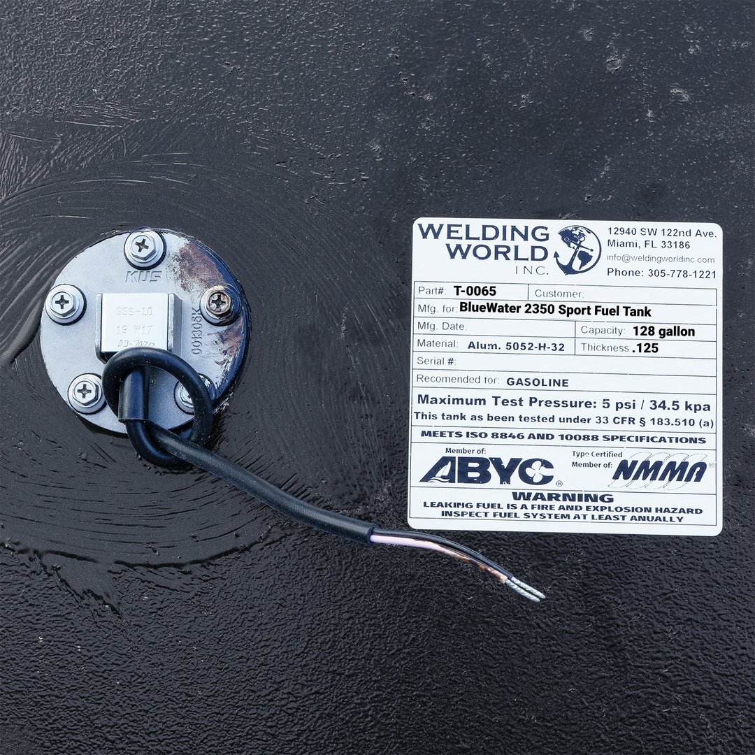 Close-up photograph of the Welding World Inc. certification label for a BlueWater 2350 Sport fuel tank, showing the 128-gallon capacity, .125" aluminum thickness, and ABYC/NMMA compliance stamps next to a KUS fuel sending unit.
