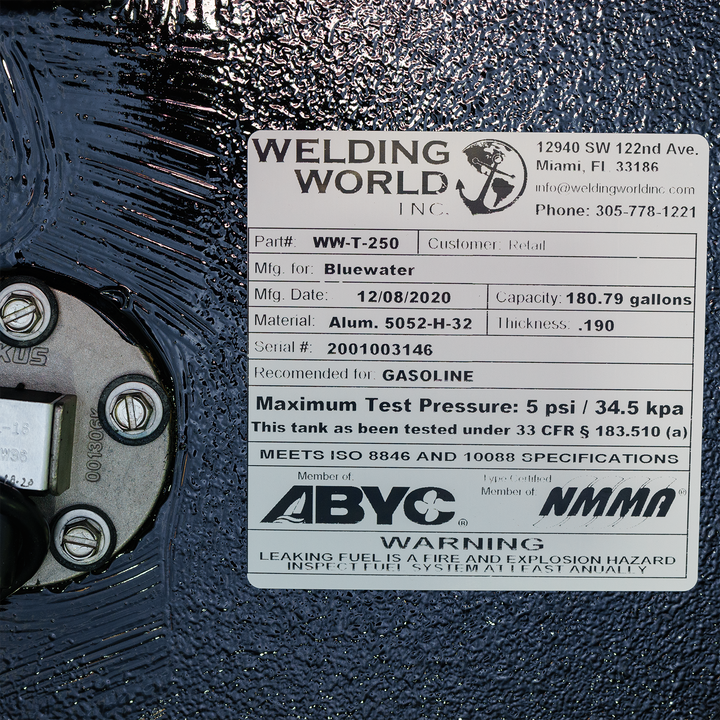 A close-up shot of a product label from "Welding World Inc." affixed to a textured black surface. The label details the product as "Part# WW-T-250," manufactured for Bluewater on December 8, 2020, with a capacity of 180.79 gallons. It specifies the material as "Alum. 5052-H-32" with a thickness of .190, serial # 2001003146, and recommended for gasoline. The label also states a maximum test pressure of 5 psi / 34.5 kpa and notes compliance with ISO 8846 and 10088 specifications, and is a member of ABYC/NMMA