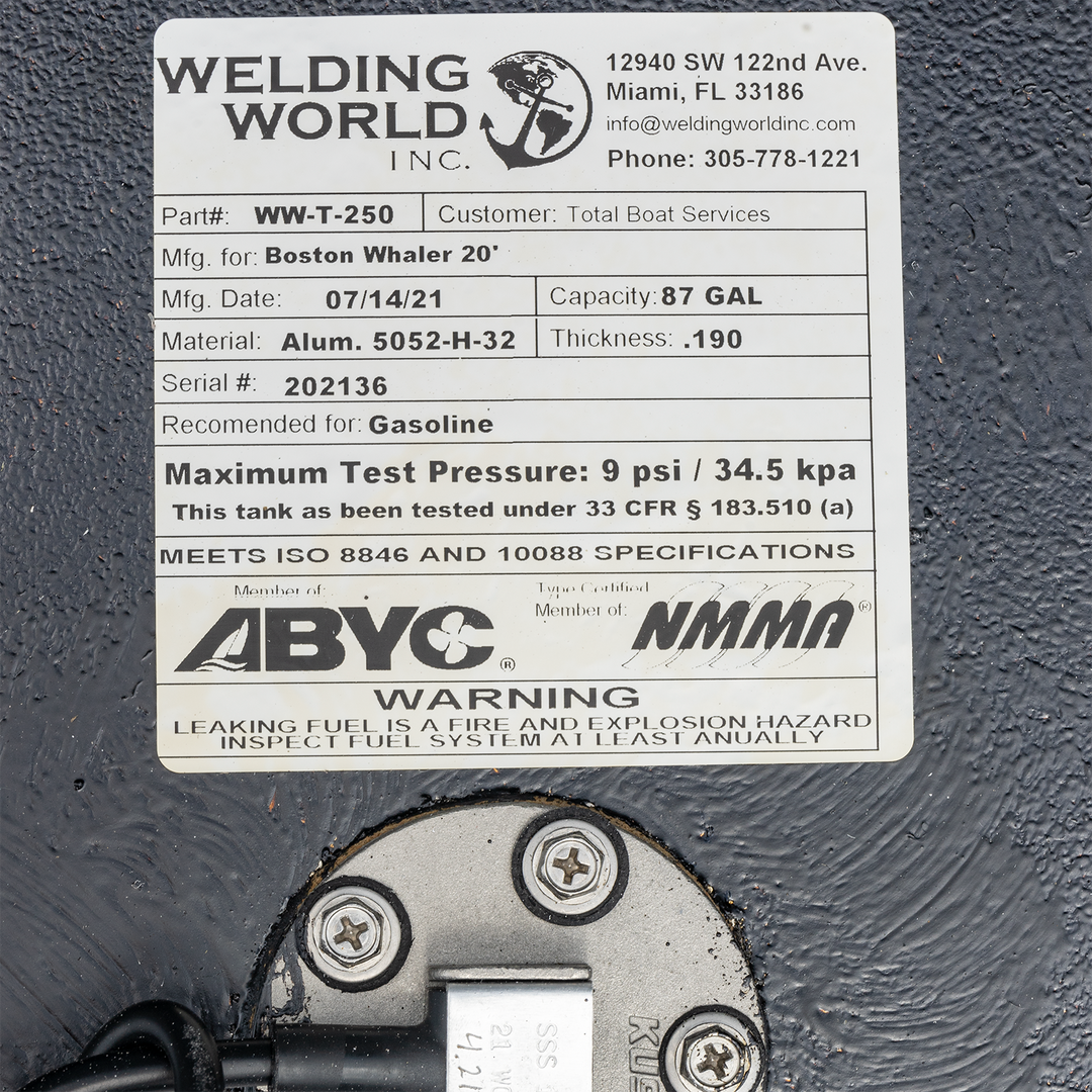 A close-up of a product label for a Welding World Inc. WW-T-250 fuel tank, customer Total Boat Services. It was manufactured on July 14, 2021, for a Boston Whaler 20', with a capacity of 87 gallons. The tank is made from 0.190-inch thick Aluminum 5052-H-32, has serial number 202136, and is recommended for gasoline. It lists a maximum test pressure of 9 psi / 34.5 kpa and states it meets 33 CFR § 183.510 (a), ISO 8846 and 10088 specifications. The label also shows memberships with ABYC and NMMA