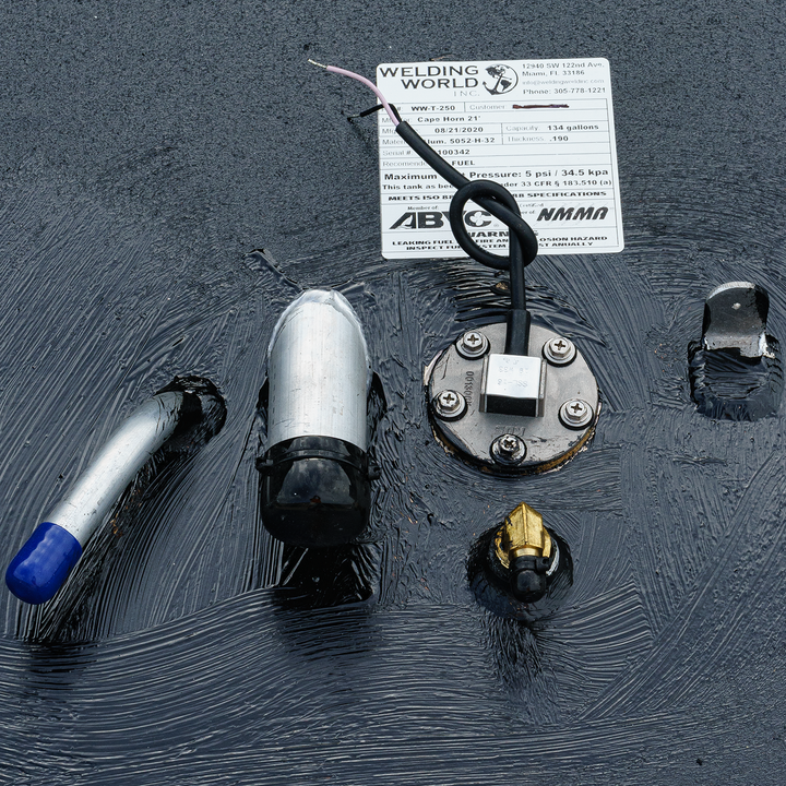 Close-up view of a 1996 Cape Horn 21' OEM replacement belly fuel tank with a 133-gallon capacity, featuring various fittings and a label from Welding World, indicating specifications and maximum pressure