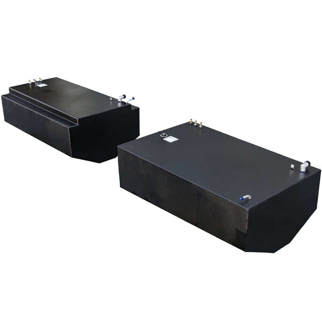 Two black fuel tanks are positioned side-by-side. The tank in the foreground is rectangular with a rounded end, while the one in the background has a raised section on its top. Both tanks feature various pipes and fitting on their top surfaces, and appear to have a textured finish