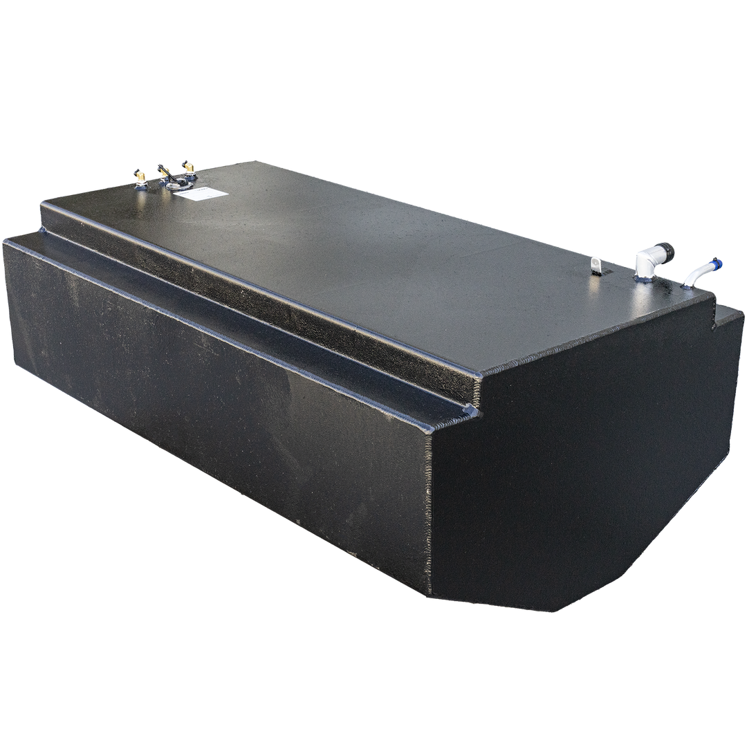 A long, black, rectangular fuel tank with a textured surface, featuring a stepped design with a raised section running along the top. The top surface shows various metal fittings, including a white L-shaped pipe with a blue tip, another white pipe, and several brass-colored connectors. The tank has a rounded front end
