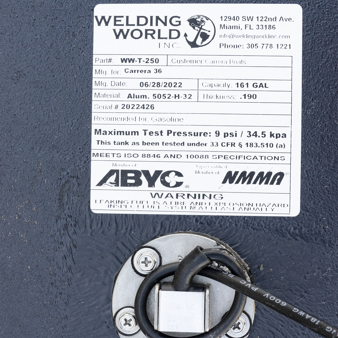 white label from Welding World Inc. attached to a black, textured fuel tank. The label provides details: Part# WW-T-250, Mfg. for Carrera 36, Mfg. Date 06/28/2022, Capacity 161 GAL, Material Alum. 5052-H-32, Thickness .190, Serial # 2022426, Recommended for Gasoline. It also states a maximum test pressure of 9 psi / 34.5 kpa, and that it meets ISO 8846 and 10088 specifications. Below the label, a circular metal fitting with wires is visible on the tank