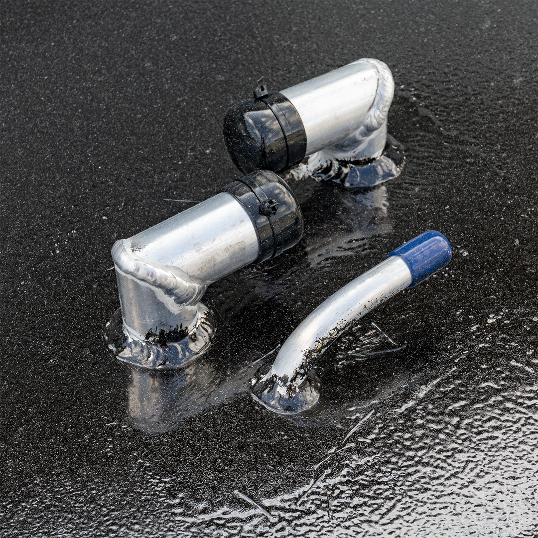 Two L-shaped silver metal pieces with black caps and a curved silver metal piece with a blue tip, all with visible welds, resting on a textured, dark, wet surface