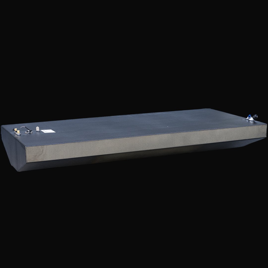 Large rectangular black fuel tank with beveled front edge and straight vertical sides, viewed from the front left corner and looking down the length of the tank. The top surface has several metal fittings clustered near the front left corner and two fittings near the back right corner. The tank shows visible weld seams and has a textured finish. Background is transparent