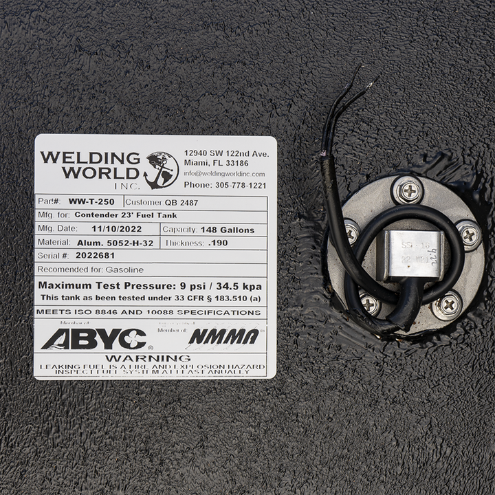 A close-up photograph shows a portion of a black textured fuel tank, focusing on a detailed manufacturer's specification label from Welding World, Inc., and an adjacent fuel sending unit. The white label specifies that the tank (part #WW-T-250, serial #2022681) was manufactured on November 10, 2022, for a Contender 23' boat. It is constructed from .190 thickness 5052-H-32 aluminum and has a capacity of 148 gallons. The label also displays ABYC and NMMA member logos and includes a safety warning
