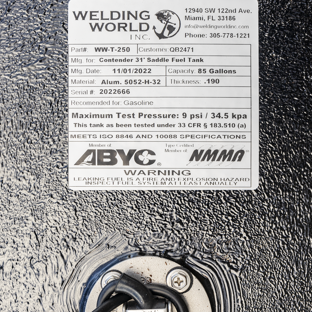A close-up view showing a white manufacturer's label positioned above a round, silver fuel sending unit on a heavily textured black surface. The "Welding World, Inc." label identifies the product as a "Contender 31' Saddle Fuel Tank" with an 85-gallon capacity, made on November 1, 2022. Below, the sending unit is recessed into the tank with a black wire emerging from its center. The label also displays ABYC and NMMA compliance logos