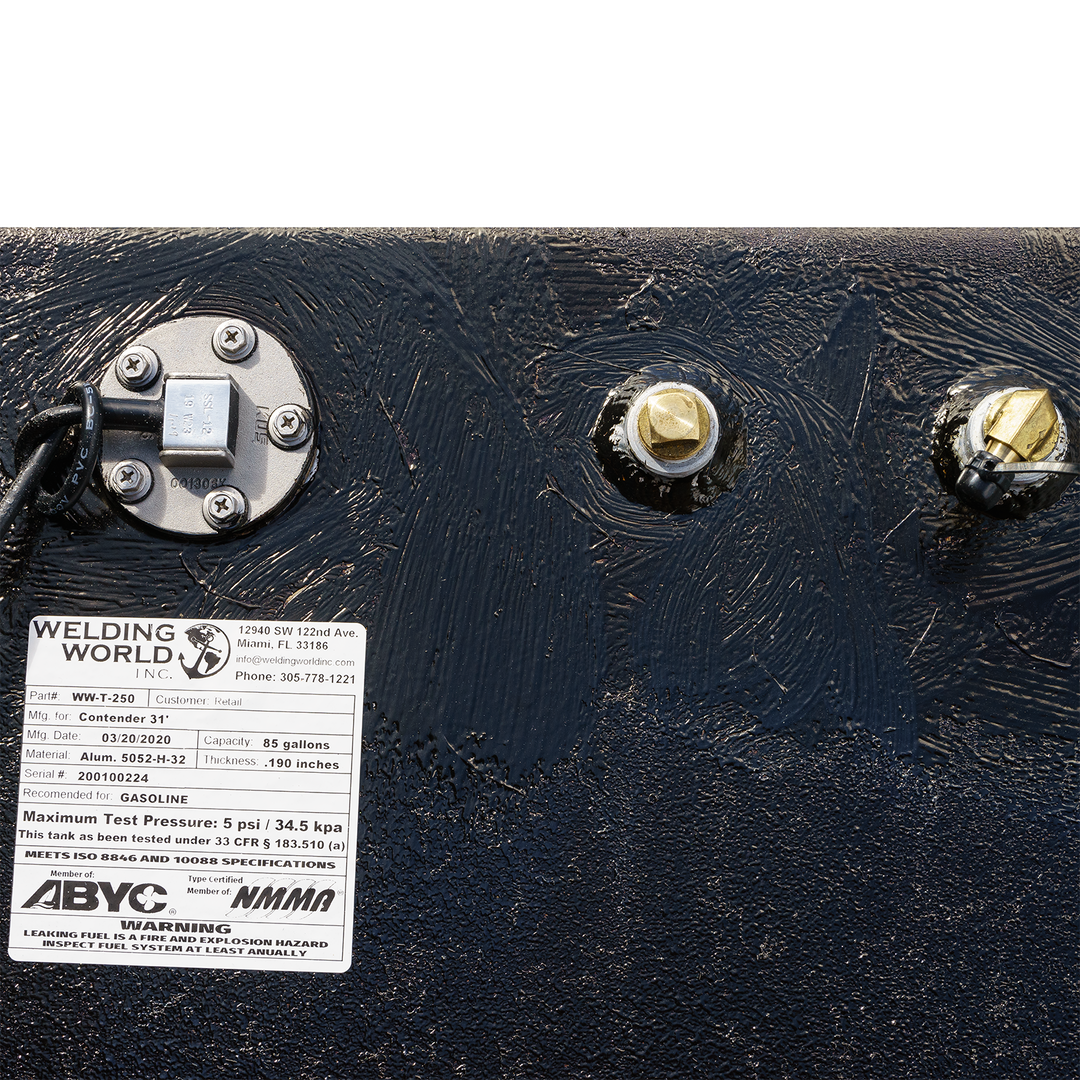 Close-up of a fuel tank assembly featuring a large belly tank with a capacity of 128 gallons, two standard saddle tanks each holding 85 gallons, and a water tank with a capacity of 21.26 gallons. The image shows the tank's fittings, including a fuel gauge and connection points, along with a label indicating specifications and safety information