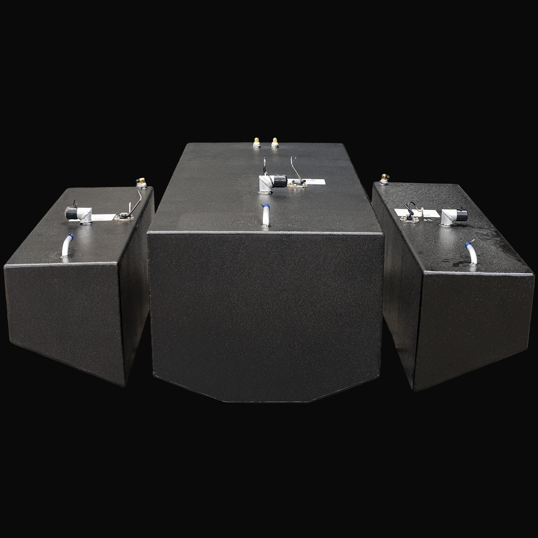 Front view of three black metal fuel tanks positioned side by side on a transparent background. The central tank is larger with a beveled front edge, flanked by two smaller rectangular tanks on each side. Each tank has metal fittings, capped openings, and wiring on top