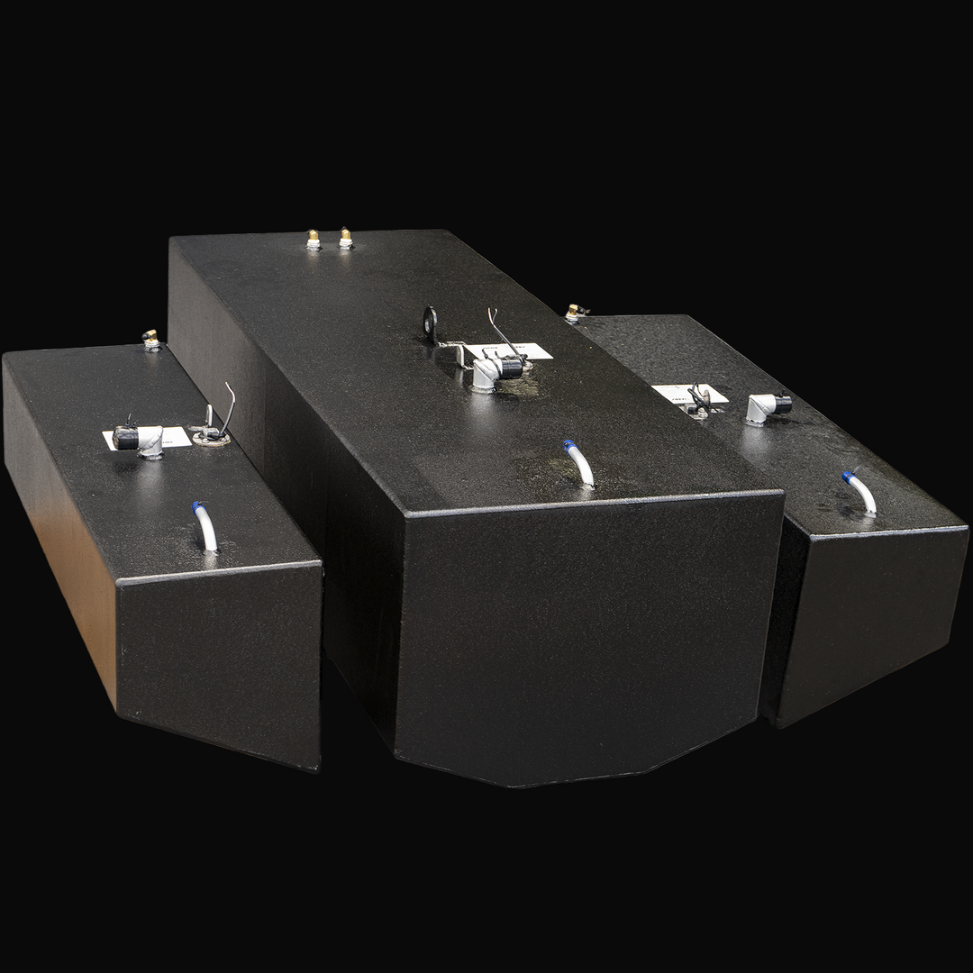 High-angle front view of three black metal fuel tanks on a transparent background. The central tank is the largest with beveled front edges, flanked by two smaller rectangular tanks on each side. Each tank has metal fittings, capped openings, wiring, and white plastic tubes on top