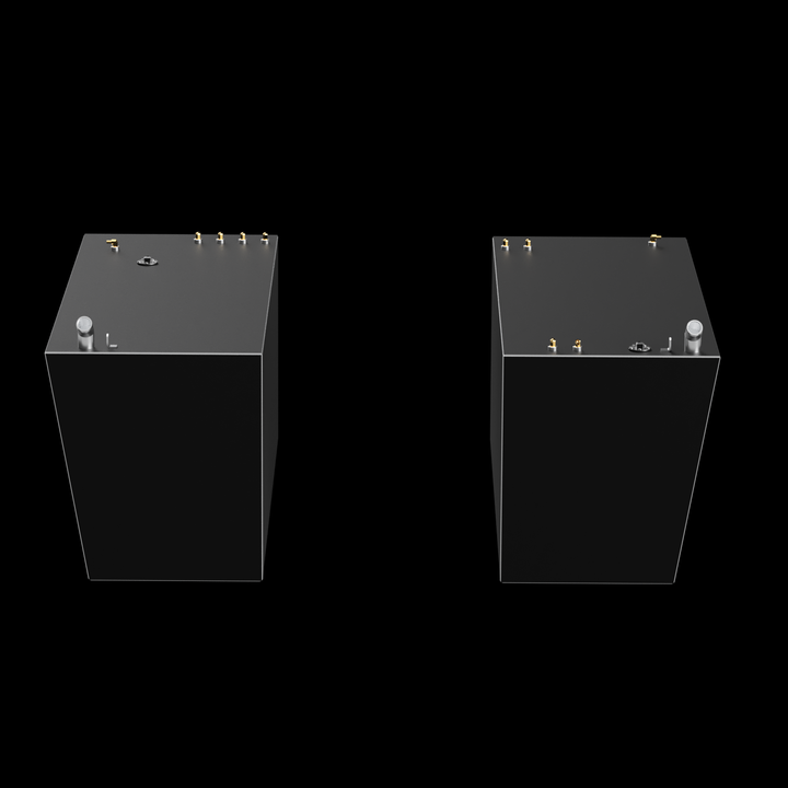 Two light gray, rectangular fuel tanks, each with a wider top surface and tapered sides, are shown against a black background. Both tanks feature various white fittings, including pipes and caps, on their top surfaces. The tanks are positioned facing each other with a gap in between