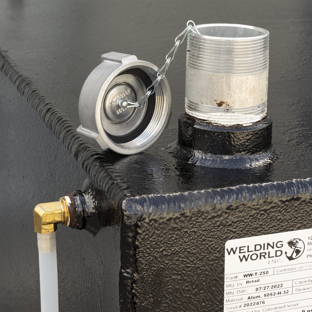 A close-up of a black, textured fuel tank with a silver threaded pipe and an attached cap via a chain on the top right. A white tube connected to a brass elbow fitting is on the top left. A white label from Welding World Inc. is visible on the side, showing details like Part# WW-T-250, Mfg Date 07/27/2022, Material Alum. 5052-H-32, and Serial# 2022476