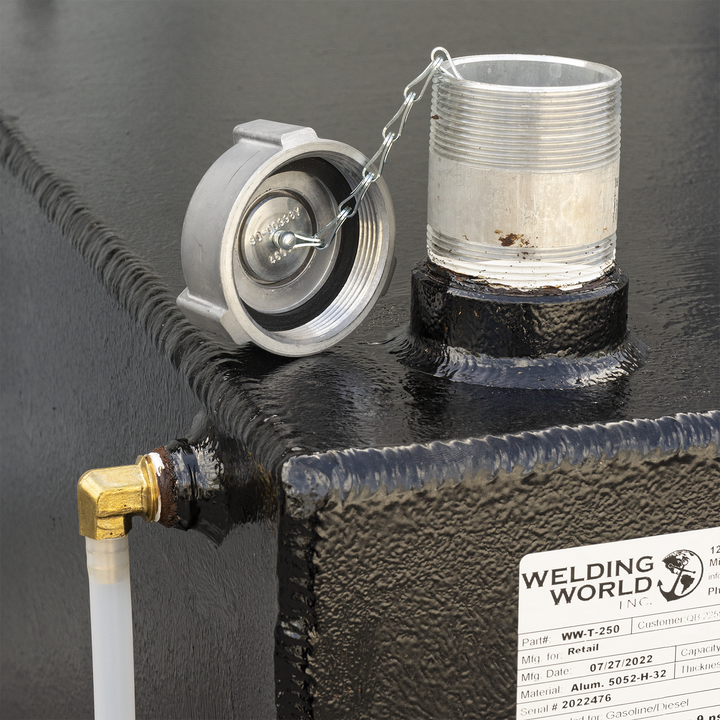 A close-up of a black, textured fuel tank with a silver threaded pipe and an attached cap via a chain on the top right. A white tube connected to a brass elbow fitting is on the top left. A white label from Welding World Inc. is visible on the side, showing details like Part# WW-T-250, Mfg Date 07/27/2022, Material Alum. 5052-H-32, and Serial# 2022476