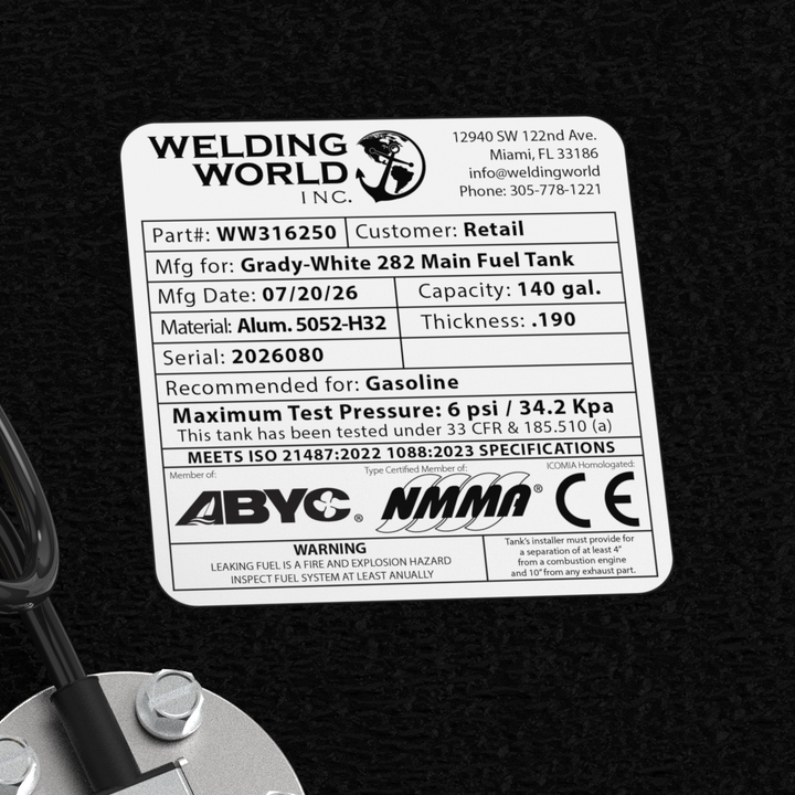 A macro top-down studio view of the top deck hardware cluster and certification label on a physical, finished black encapsulated Grady-White 282 Sailfish Main OEM replacement fuel tank (140 gal) from file image_f14b58.jpg. Positioned against the textured black TarGard epoxy coating, the hardware includes a central circular silver KUS electronic fuel level sending unit fastened with five bolts and fitted with a coiled black wiring lead. Surrounding the sender are dual pre-installed high-flow brass 90-degree 
