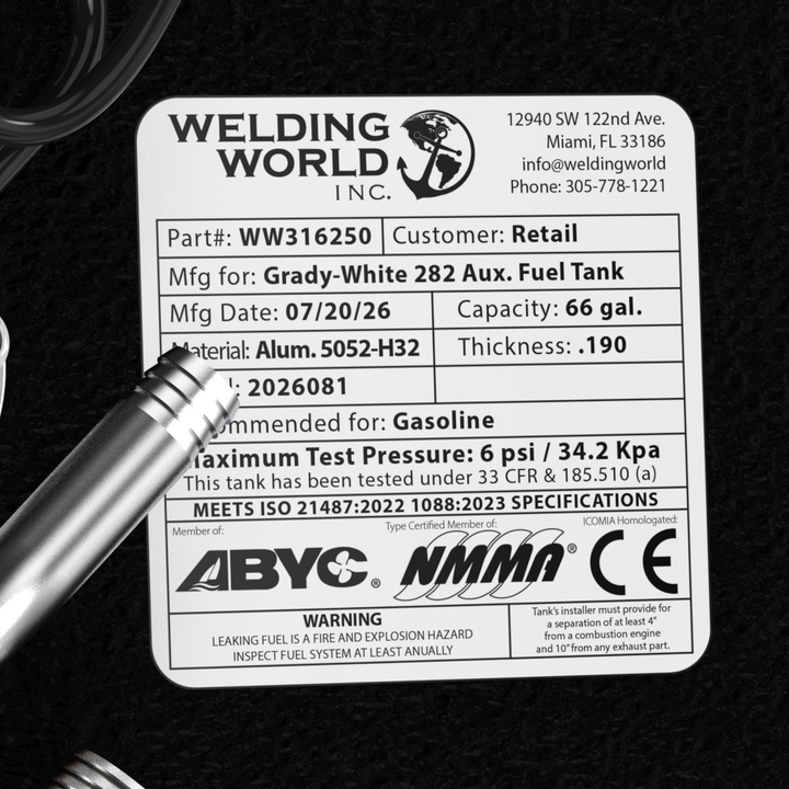 A macro top-down studio view of the complete top deck hardware cluster and certification label on a physical, finished black encapsulated Grady-White 282 Sailfish Auxiliary OEM replacement fuel tank (66 gal) from file image_f14e63.jpg. Positioned against the textured black TarGard epoxy coating, the assembly features a central circular silver KUS electronic fuel level sending unit secured with five bolts and a coiled black wire harness. Adjacent fittings include a pre-welded 90-degree aluminum fuel fill nec