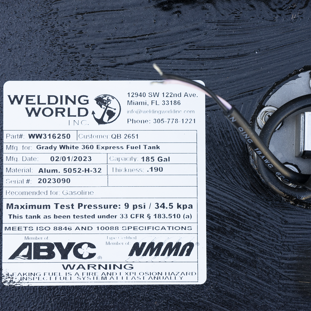 Close-up of the manufacturer's label on a Grady-White 360 Express fuel tank made by Welding World Inc., Miami, FL. The label shows part number WW316250, customer QB 2651, 185-gallon capacity, manufactured on 02/01/2023, made from 0.190-inch thick aluminum 5052-H-32. Serial number 2023090. Certified for gasoline, tested to 9 psi under 33 CFR § 183.510(a), and compliant with ISO 8846 and 10088. ABYC and NMMA certification logos and a safety warning are visible