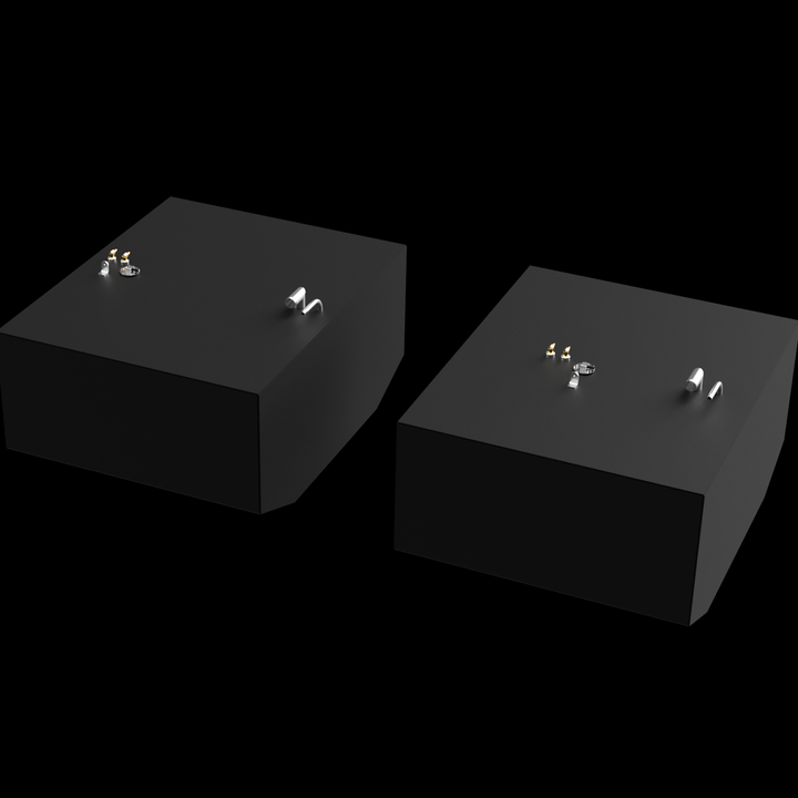 Two dark grey, rectangular fuel tanks are shown from an elevated, angled perspective against a black background with subtle white dots. Each tank has various golden and silver-colored fittings on its top surface, including pipes and valves. The tank in the foreground has a rounded bottom corner, while the tank in the background has angled bottom corners