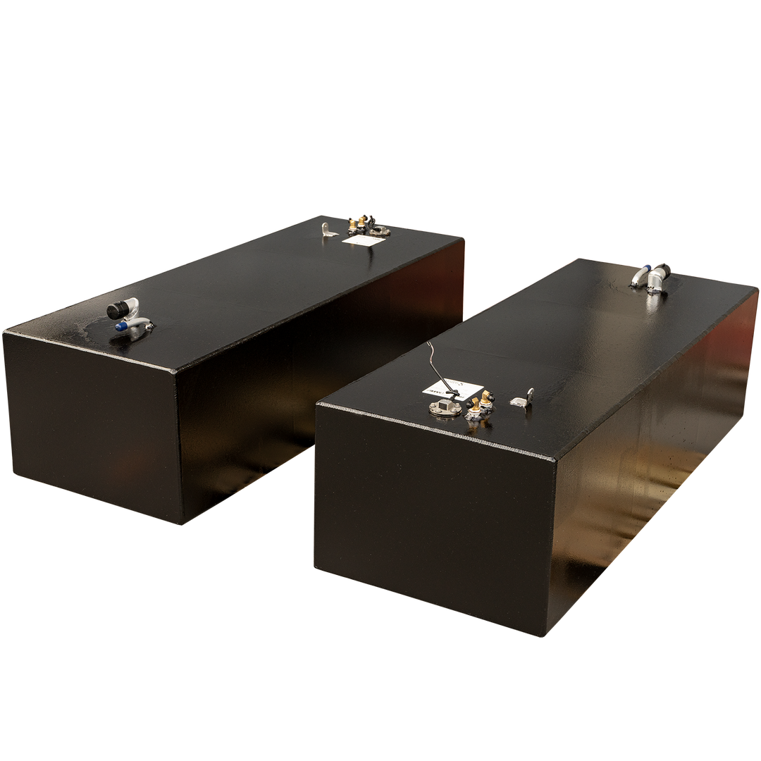 Two sleek, rectangular black fuel tanks, each equipped with various pipe connections, gauges, and fittings on their top surfaces, are positioned at an angle against a black and grey checkered background. The tanks appear to have a glossy finish