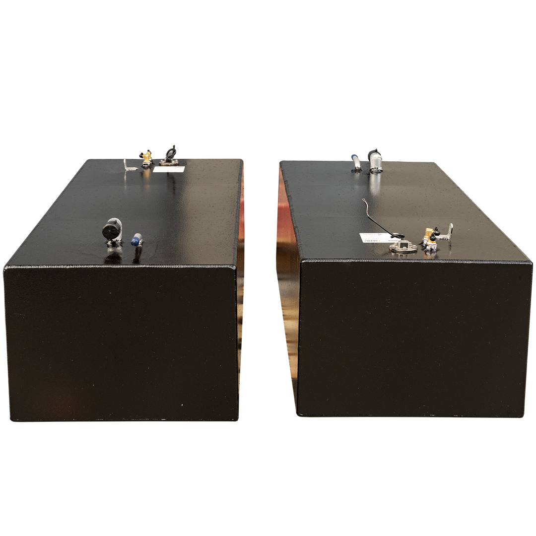 Two rectangular black fuel tanks are positioned side-by-side with a gap between them, against a black and grey checkered background. Both tanks feature various fittings and connections on their top surfaces, including white and blue pipes, and circular gauges with wires