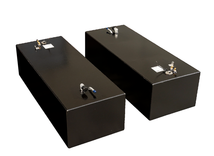 Two rectangular black fuel tanks, viewed from an elevated angle against a checkered background. Both tanks feature various metallic fittings and pipes on their top surfaces, including a white and blue pipe, and a circular gauge with wires. The tank in the foreground has a more prominent view of the white and blue pipe, while the tank in the background prominently displays the circular gauge and other smaller fittings