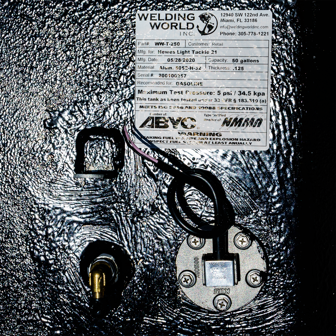 Close-up of a 1994 Hewes Light Tackle 21' belly fuel tank with a 56-gallon capacity. The tank features a label from Welding World, Inc., detailing customer information and specifications, including a maximum test pressure of 5 psi. The tank is equipped with a fuel gauge and a fuel line connection