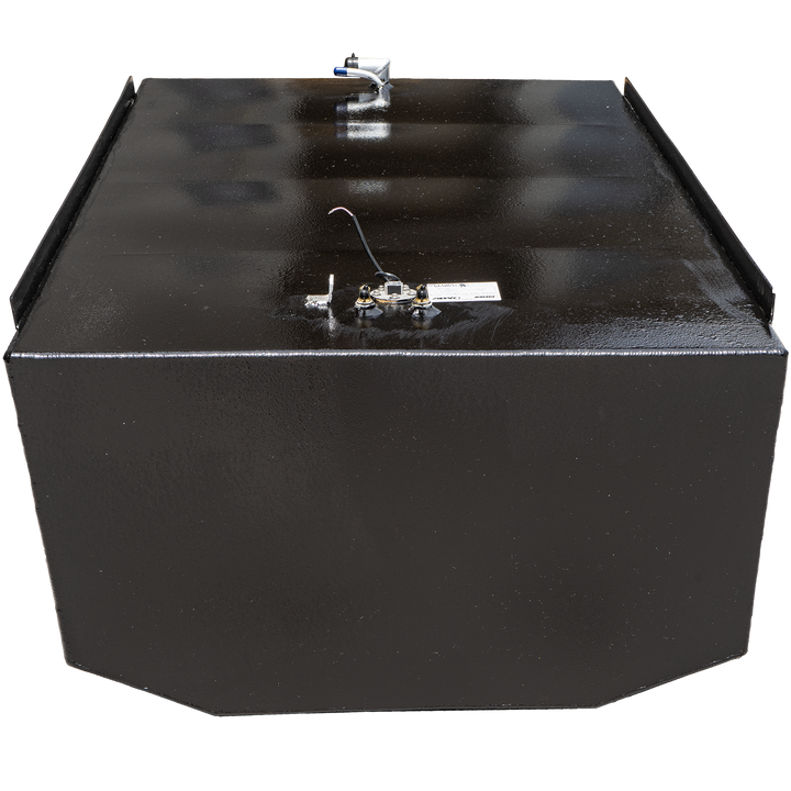 A black, rectangular fuel tank with a textured surface, shown against a black and grey checkered background. Various metallic and plastic fittings, including a white and blue tube and brass-colored connectors, are visible on its top surface, along with a small white label. A black strip runs along the top edges, creating a lip