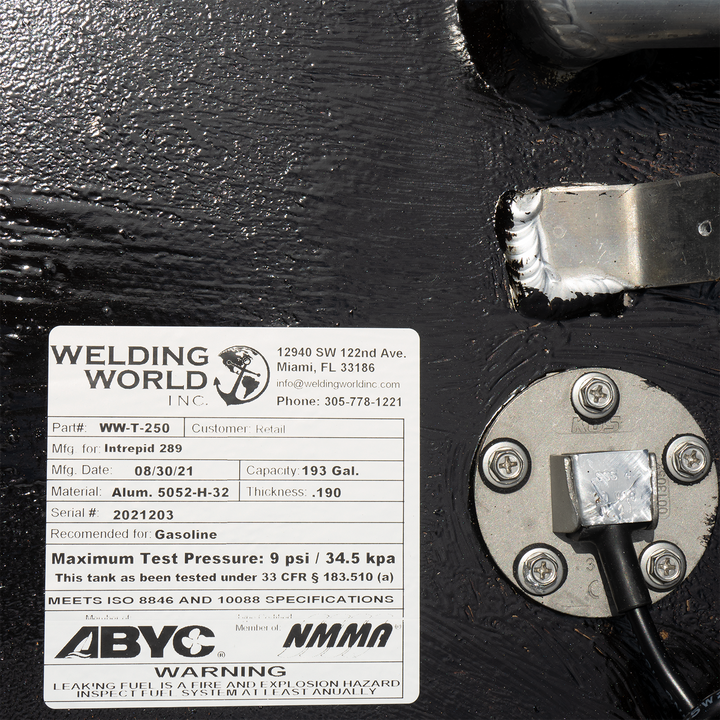 A label on a black fuel tank for an Intrepid 289, indicating it is a 193-gallon main fuel tank manufactured by Welding World Inc. on 08/30/21. The label includes the part number WW-T-250, material as Alum. 5052-H-32 with a thickness of .190, serial number 2021203, and states it is recommended for gasoline with a maximum test pressure of 9 psi / 34.5 kpa. It also notes that the tank meets ISO 8846 and 10088 specifications and is certified by ABYC and NMMA, with a warning about leaking fuel