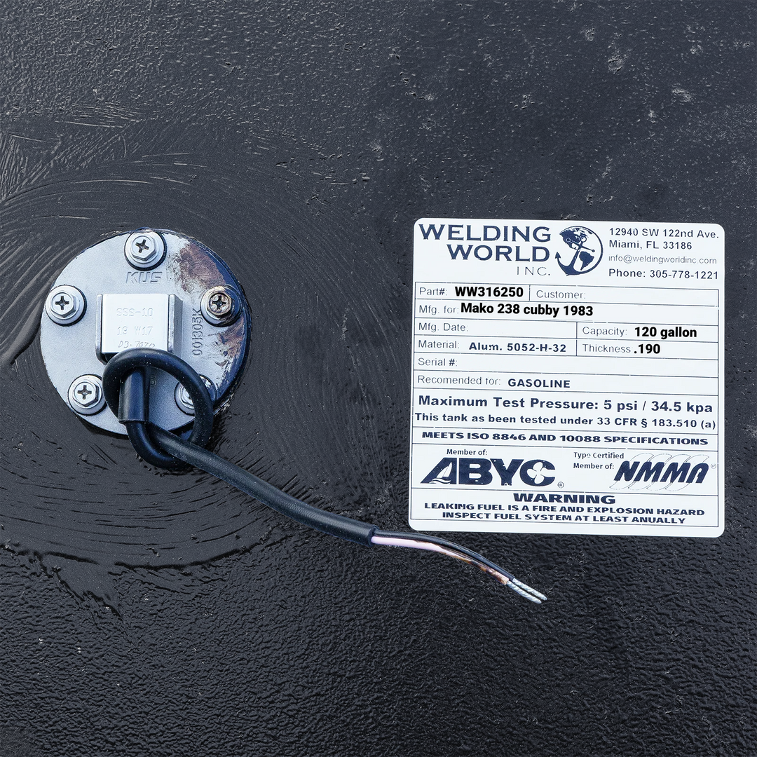 Close-up photograph of the manufacturing label for a 120-gallon Mako 238 Cubby fuel tank by Welding World Inc., detailing the .190" thickness and 5052-H32 aluminum specs, positioned next to a stainless steel KUS fuel sending unit on a coal-tar epoxy finish.