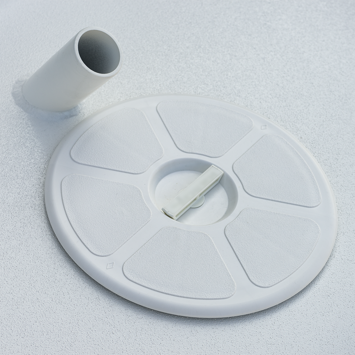 A white circular high flotation bracket with a central locking latch, and a separate cylindrical pipe component, both placed on a textured white surface. The bracket appears to be part of a marine or boat assembly system