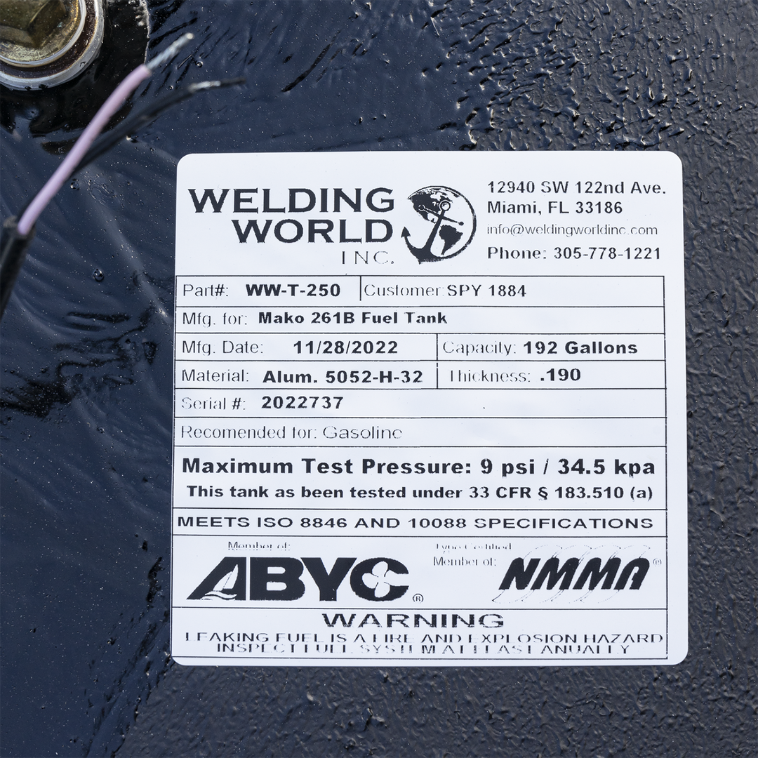 A close-up photograph of a white manufacturer's label on a black fuel tank. The label is for "Welding World, Inc." and details the specifications for a "Mako 261B Fuel Tank." Key information listed includes a 192-gallon capacity, an aluminum material type, a manufacturing date of 11/28/2022, and a serial number. The label also displays compliance logos for ABYC and NMMA, pressure testing data, and a safety warning at the bottom. The edge of a fuel fitting and a wire are visible in the upper left corner.
