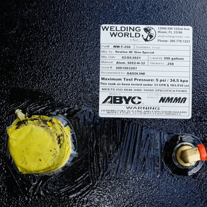 A close-up of the Newton 46' Dive Special - 200 gal. OEM Replacement Diesel Saddle Tank's information label, detailing specifications like part number (WW-T-250), manufacturing date (02/05/2021), capacity (200 gallons), material (Alum. 5052-H-32), and thickness (.250). It also indicates the tank is recommended for gasoline, has a maximum test pressure of 5 psi / 34.5 kpa, and meets ISO 8846 and 10088 specifications. The label includes a warning about leaking fuel and advises annual inspection