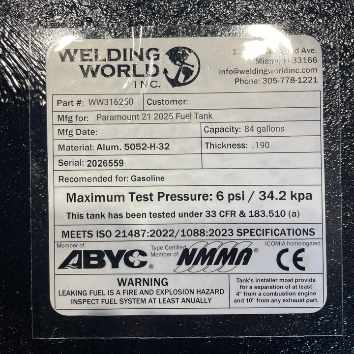 A close-up studio detail view of the official manufacturer specification and compliance certification plate applied directly to the textured black TarGard epoxy finish of a finished Paramount 21 2025 OEM replacement marine fuel tank (84 gal) from file image_c21482.jpg. Certified by Welding World Inc. in Miami, FL, the spec plate confirms part number WW316250, serial number 2026559, heavy-duty .190-thickness marine-grade Alum. 5052-H-32 construction, gasoline compatibility, 6 psi / 34.2 kPa maximum pressure 