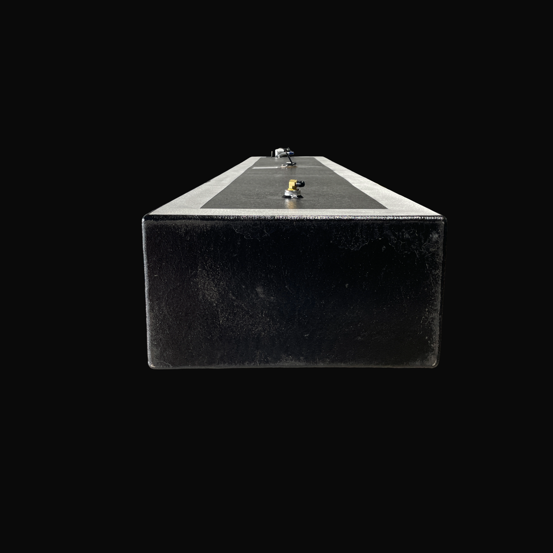 A studio rear-facing end perspective view looking down the length of a physical, finished black encapsulated Proline 21 OEM replacement marine fuel tank (84 gal 1994) from file image_15221d.jpg, isolated against a black background. Precision-fabricated from heavy-gauge marine-grade 5052-H32 aluminum, the long rectangular body is fully encapsulated in a protective, textured black TarGard epoxy coating with bare aluminum border margins along the top deck edges. The top deck configuration highlights a foregrou