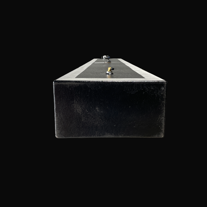 A studio rear-facing end perspective view looking down the length of a physical, finished black encapsulated Proline 21 OEM replacement marine fuel tank (84 gal 1994) from file image_15221d.jpg, isolated against a black background. Precision-fabricated from heavy-gauge marine-grade 5052-H32 aluminum, the long rectangular body is fully encapsulated in a protective, textured black TarGard epoxy coating with bare aluminum border margins along the top deck edges. The top deck configuration highlights a foregrou