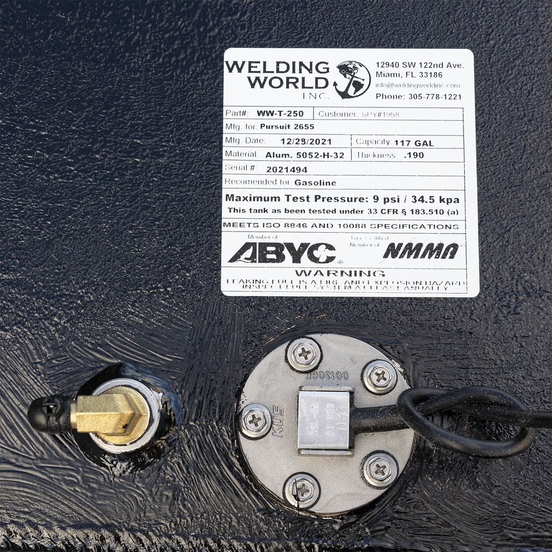 A white product label for a fuel tank from "WELDING WORLD INC." is affixed to a black, textured surface. The label details the tank's specifications: Part # WW-T-250, Mfg. for Pursuit 2655, Mfg. Date: 12/29/2021, Capacity: 117 GAL, Material: Alum. 5052-H-32, Thickness: .190, Serial #: 2021494. It is recommended for Gasoline and has a Maximum Test Pressure of 9 psi / 34.5 kpa. The tank meets ISO 8846 and 10088 SPECIFICATIONS and is certified by ABYC and NMMA. A warning about leaking fuel is also present