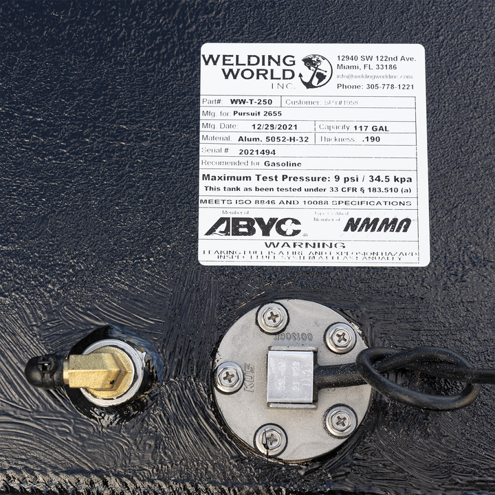 A white product label for a fuel tank from "WELDING WORLD INC." is affixed to a black, textured surface. The label details the tank's specifications: Part # WW-T-250, Mfg. for Pursuit 2655, Mfg. Date: 12/29/2021, Capacity: 117 GAL, Material: Alum. 5052-H-32, Thickness: .190, Serial #: 2021494. It is recommended for Gasoline and has a Maximum Test Pressure of 9 psi / 34.5 kpa. The tank meets ISO 8846 and 10088 SPECIFICATIONS and is certified by ABYC and NMMA. A warning about leaking fuel is also present